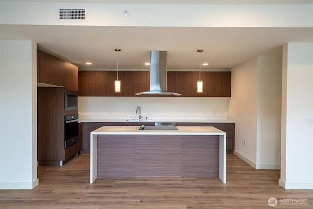 kitchen with visible vents, island range hood, modern cabinets, oven, and a sink