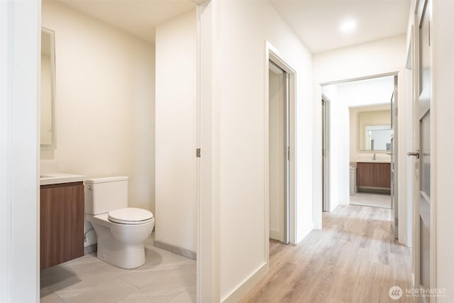 half bath with toilet, baseboards, wood finished floors, and vanity