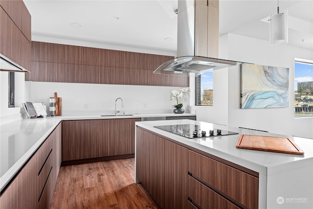 kitchen with black electric stovetop, island range hood, sink, pendant lighting, and light hardwood / wood-style flooring