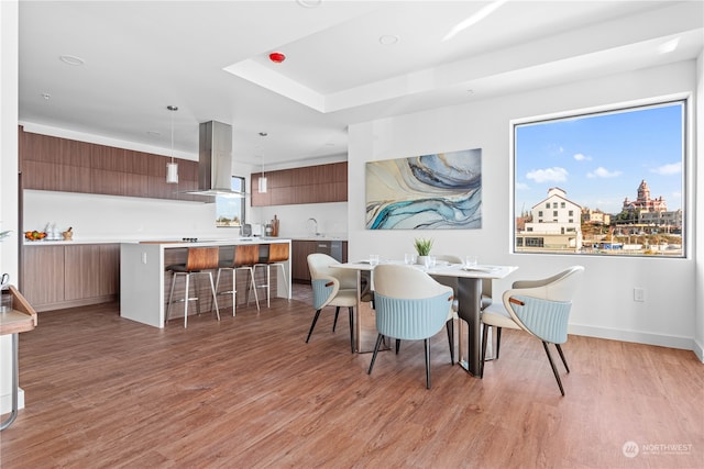 dining area with a raised ceiling, sink, and light hardwood / wood-style floors