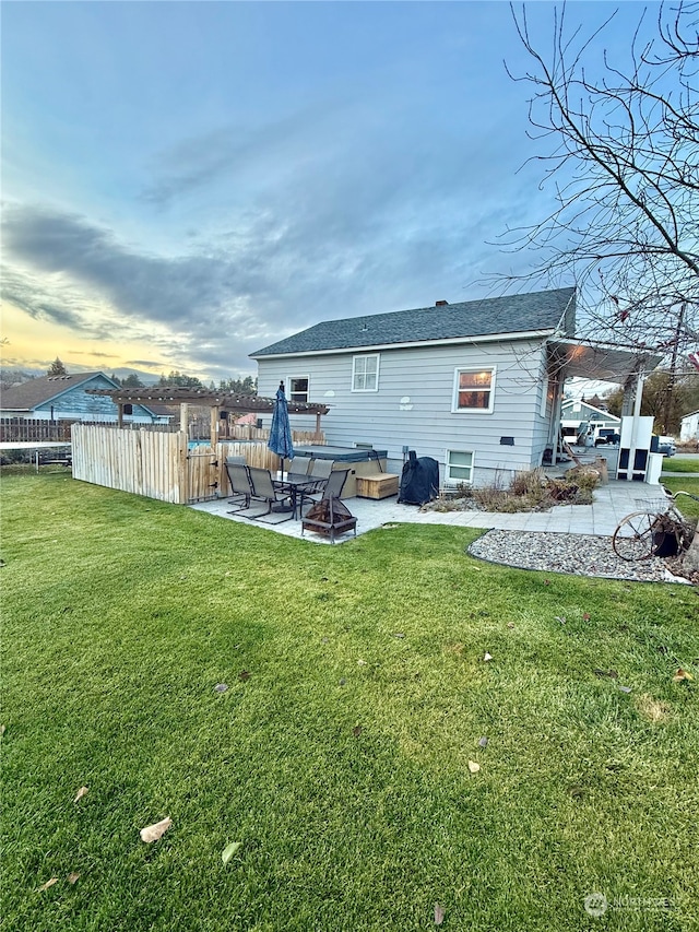 back house at dusk featuring a patio area and a lawn