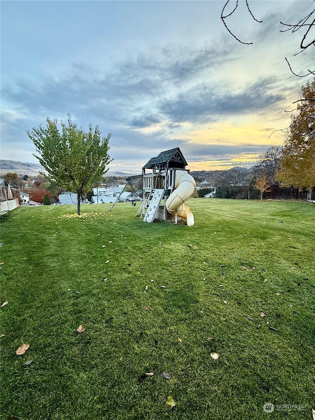 yard at dusk featuring a playground and a water view