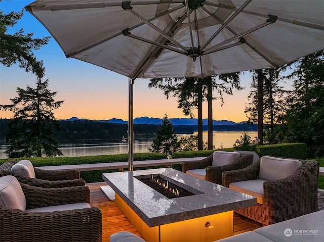 patio terrace at dusk with a deck with water view and a fire pit