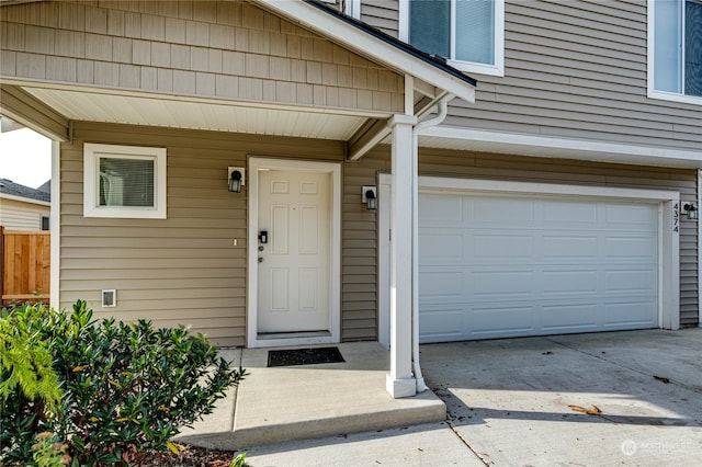 property entrance with concrete driveway, an attached garage, and fence