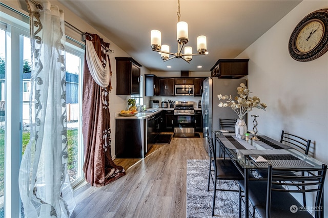 kitchen featuring appliances with stainless steel finishes, decorative light fixtures, light wood-type flooring, dark brown cabinetry, and an inviting chandelier