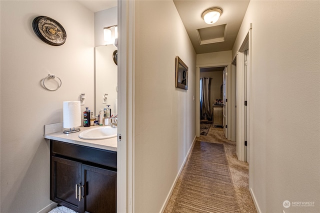 corridor featuring carpet flooring, a sink, attic access, and baseboards