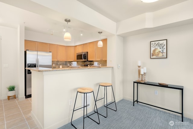 kitchen featuring decorative backsplash, kitchen peninsula, light stone countertops, stainless steel appliances, and decorative light fixtures