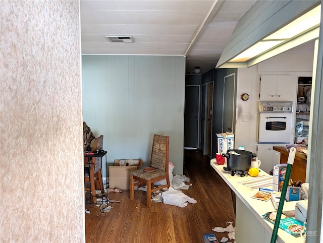 kitchen with white oven, white cabinetry, wooden walls, and dark wood-type flooring