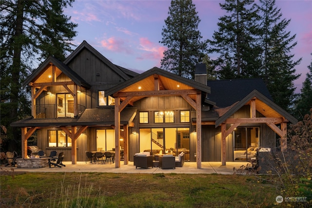 back house at dusk featuring an outdoor living space with a fire pit, a patio area, and a balcony