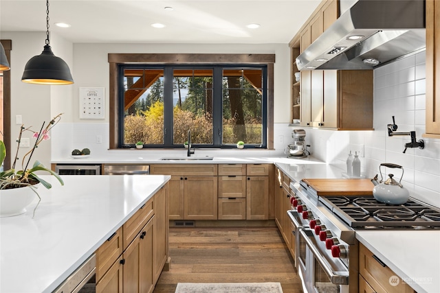 kitchen featuring wall chimney range hood, stainless steel stove, pendant lighting, sink, and dark wood-type flooring