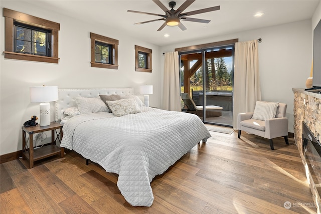 bedroom featuring a stone fireplace, access to outside, wood-type flooring, and ceiling fan