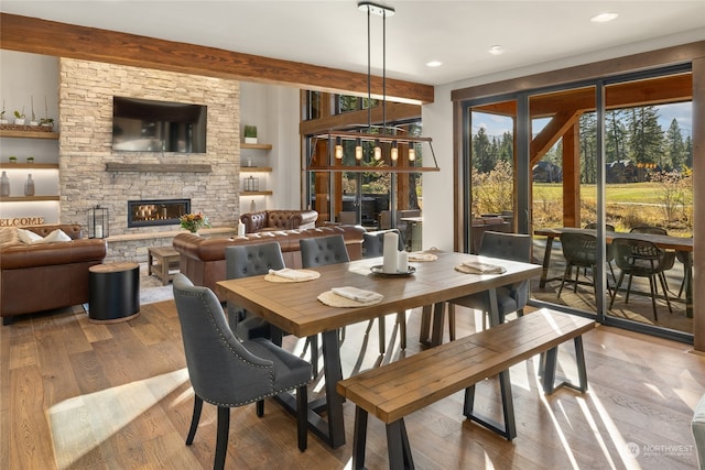 dining room with a stone fireplace, hardwood / wood-style floors, and beam ceiling