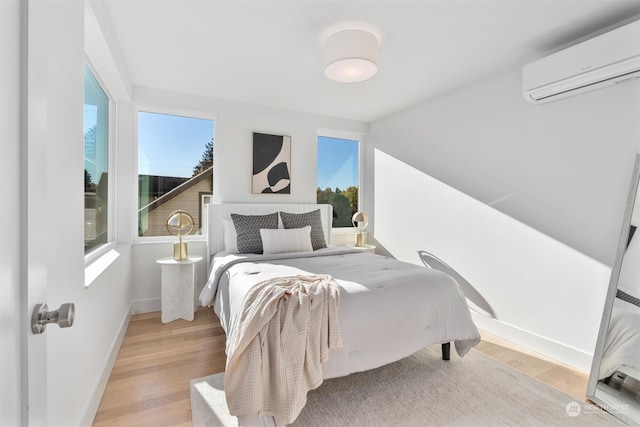 bedroom with multiple windows, light hardwood / wood-style floors, and an AC wall unit