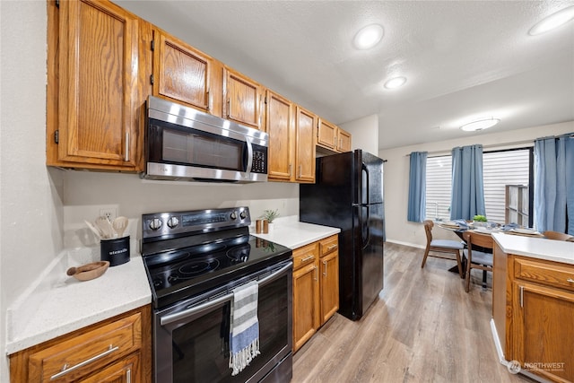 kitchen featuring light wood-type flooring, a textured ceiling, and black appliances