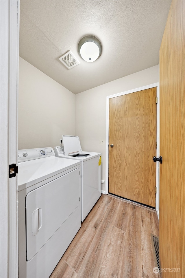 clothes washing area with light hardwood / wood-style floors, separate washer and dryer, and a textured ceiling