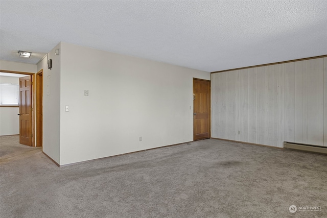 empty room featuring a baseboard heating unit, light colored carpet, wooden walls, and a textured ceiling