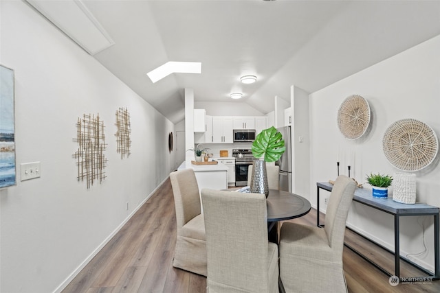 dining room with vaulted ceiling with skylight and light hardwood / wood-style flooring