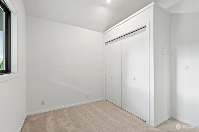 unfurnished bedroom with light colored carpet, vaulted ceiling, and a closet