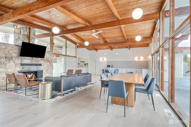 dining room featuring a stone fireplace, light hardwood / wood-style flooring, beamed ceiling, and wood ceiling