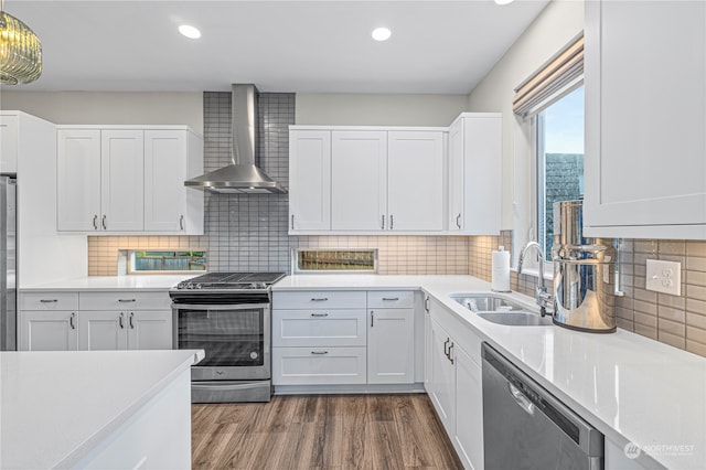 kitchen with white cabinetry, wall chimney range hood, appliances with stainless steel finishes, dark hardwood / wood-style flooring, and sink