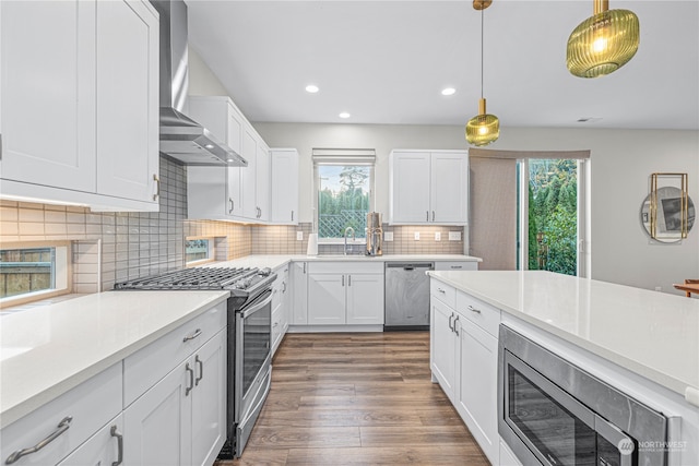 kitchen featuring pendant lighting, a wealth of natural light, wall chimney exhaust hood, and stainless steel appliances