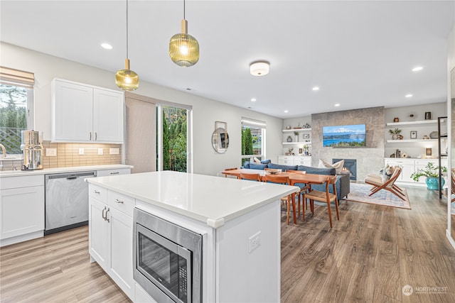 kitchen with white cabinets, a fireplace, appliances with stainless steel finishes, and light hardwood / wood-style floors