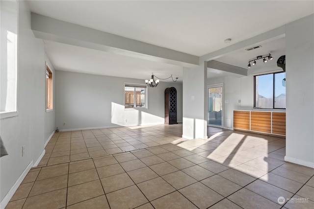 spare room with track lighting, plenty of natural light, a chandelier, and light tile patterned flooring