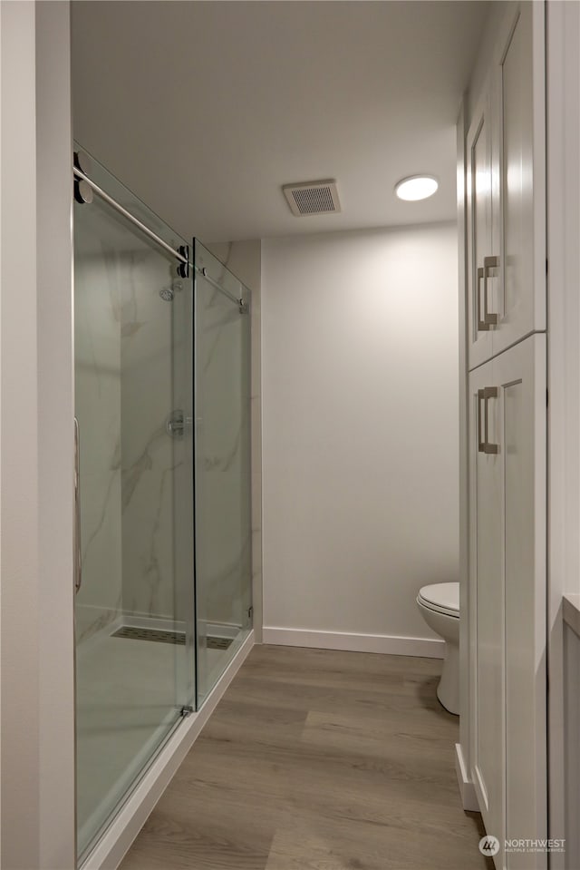 bathroom with an enclosed shower, wood-type flooring, and toilet