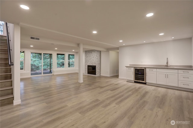 unfurnished living room featuring wine cooler, a stone fireplace, indoor wet bar, and light hardwood / wood-style flooring