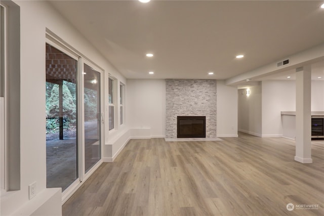 unfurnished living room featuring a stone fireplace, wine cooler, and light hardwood / wood-style flooring