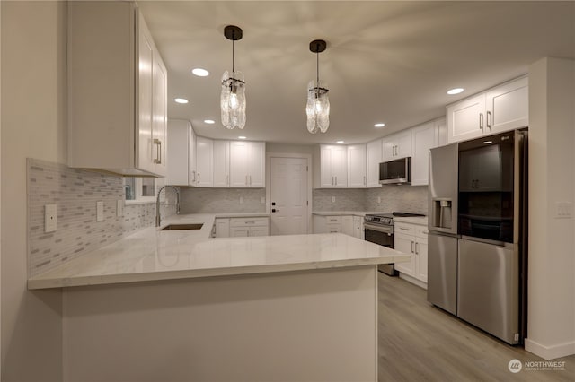 kitchen with stainless steel appliances, sink, white cabinets, kitchen peninsula, and light hardwood / wood-style flooring