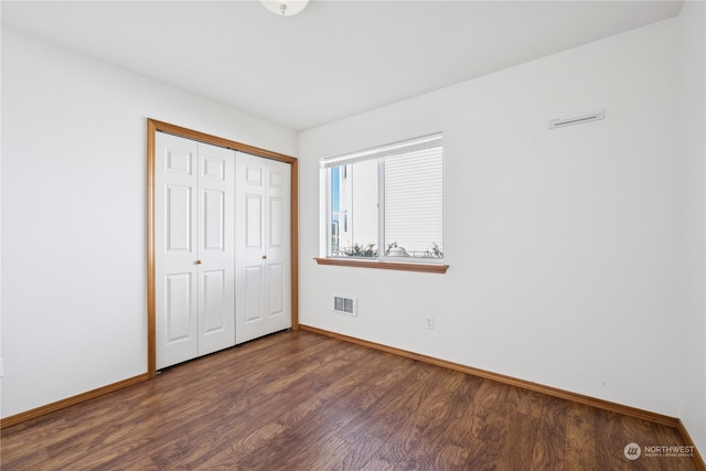 unfurnished bedroom with a closet, visible vents, dark wood-type flooring, and baseboards