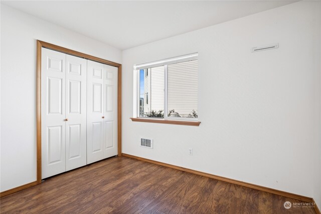 unfurnished bedroom with dark wood-style floors, visible vents, baseboards, and a closet