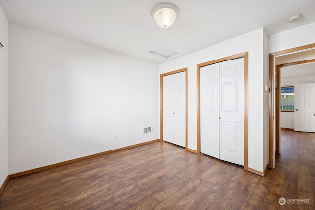 unfurnished bedroom with baseboards, visible vents, attic access, dark wood-style flooring, and two closets