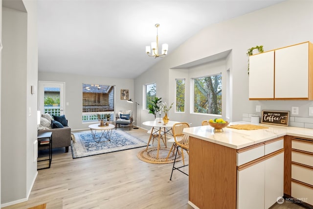 kitchen featuring light hardwood / wood-style floors, vaulted ceiling, white cabinets, kitchen peninsula, and decorative light fixtures