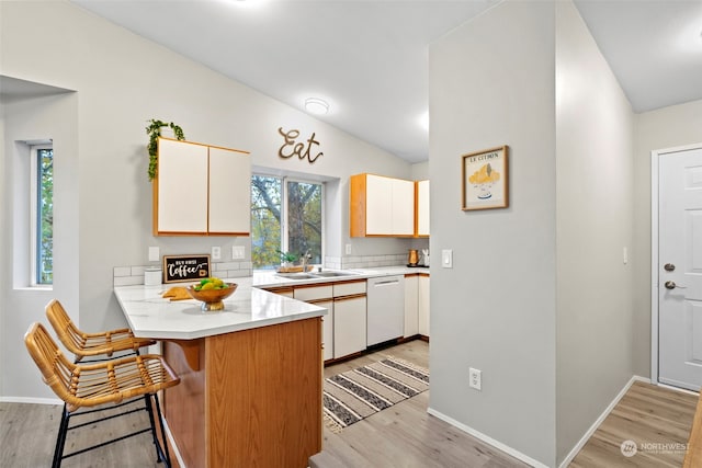 kitchen with light hardwood / wood-style floors, sink, kitchen peninsula, white dishwasher, and lofted ceiling