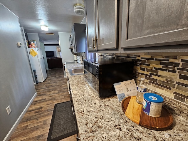 kitchen with decorative backsplash, white fridge, light stone countertops, and dark hardwood / wood-style floors