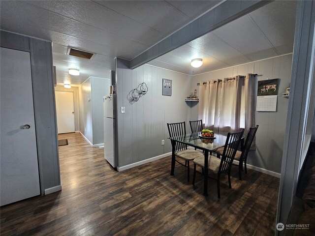 dining room with beam ceiling, wooden walls, and dark hardwood / wood-style floors