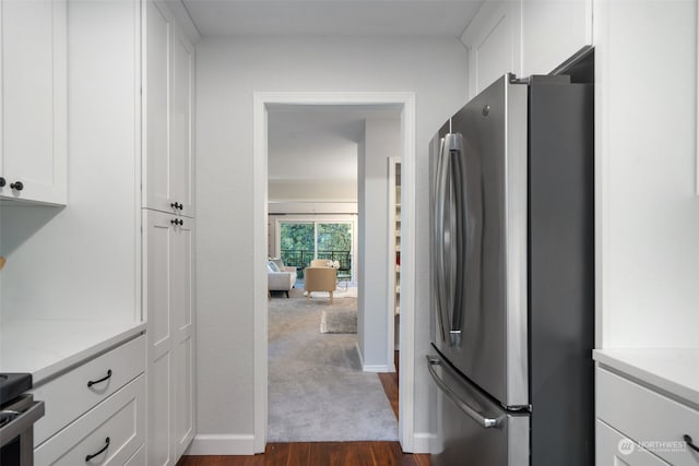 kitchen featuring dark wood-type flooring, light stone countertops, stainless steel refrigerator, and white cabinetry