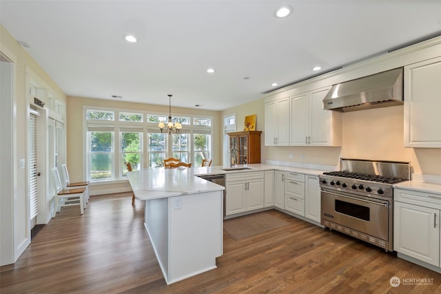 kitchen with luxury stove, wall chimney exhaust hood, dark hardwood / wood-style floors, decorative light fixtures, and kitchen peninsula