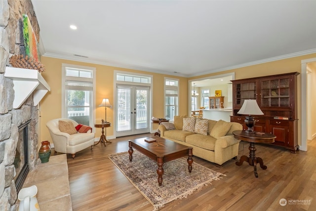 living room featuring light hardwood / wood-style floors, crown molding, a fireplace, and french doors