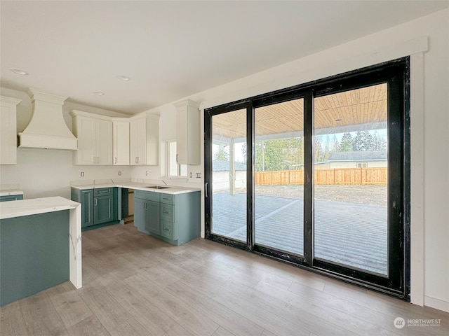 kitchen with custom range hood, sink, white cabinets, light hardwood / wood-style floors, and green cabinets