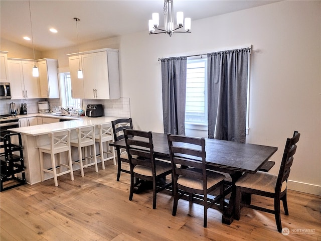 dining space with light hardwood / wood-style flooring, a chandelier, sink, and vaulted ceiling