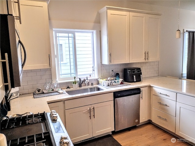 kitchen featuring stainless steel appliances, sink, hanging light fixtures, light hardwood / wood-style flooring, and decorative backsplash