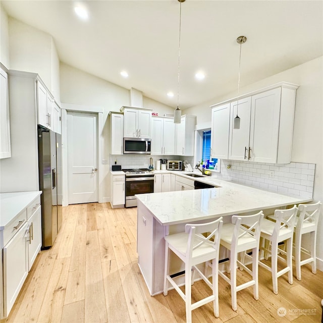 kitchen with white cabinetry, kitchen peninsula, appliances with stainless steel finishes, a kitchen breakfast bar, and hanging light fixtures