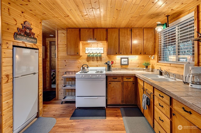 kitchen with wood walls, white appliances, sink, and light hardwood / wood-style flooring