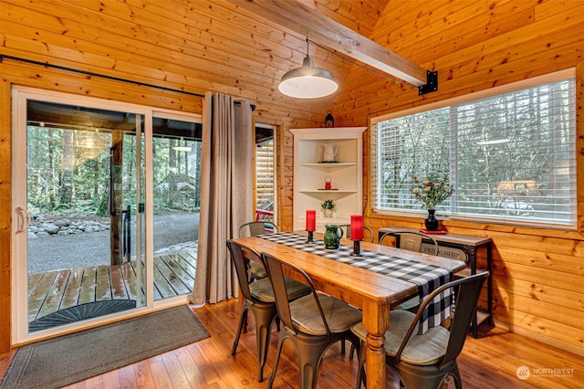 dining room with wood walls, plenty of natural light, light wood-type flooring, and vaulted ceiling with beams