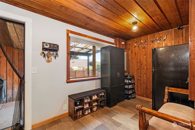 bedroom featuring light wood-type flooring, freestanding refrigerator, wooden ceiling, and wood walls