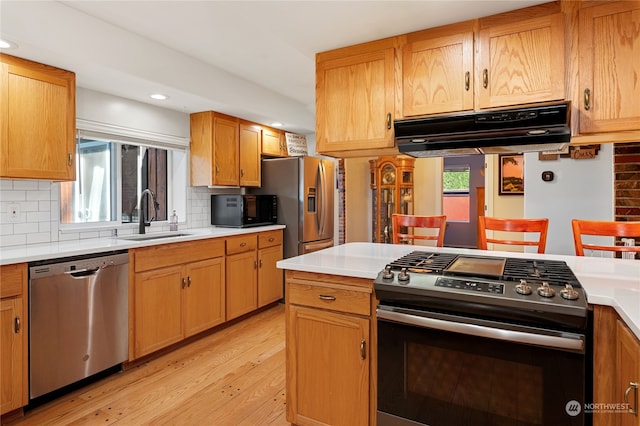 kitchen featuring stainless steel appliances, tasteful backsplash, light countertops, a sink, and under cabinet range hood