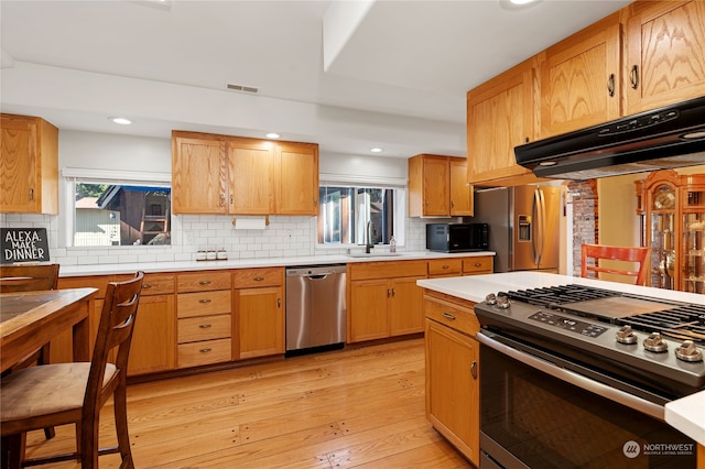 kitchen featuring stainless steel appliances, light countertops, light wood-type flooring, under cabinet range hood, and a sink